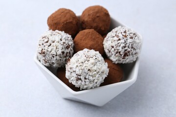 Delicious homemade candies with cocoa powder and coconut flakes in bowl on white table, closeup