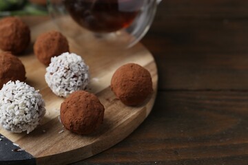 Delicious homemade candies with cocoa powder and coconut flakes on wooden table, closeup. Space for...