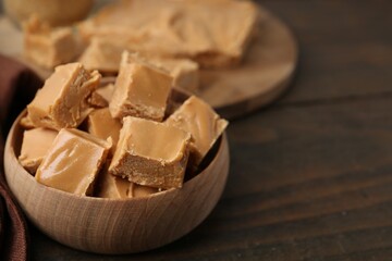 Homemade caramel candies in bowl on wooden table, closeup. Space for text