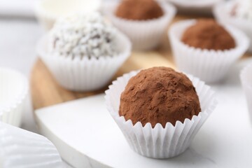 Delicious homemade candies with cocoa powder and coconut flakes on table, closeup