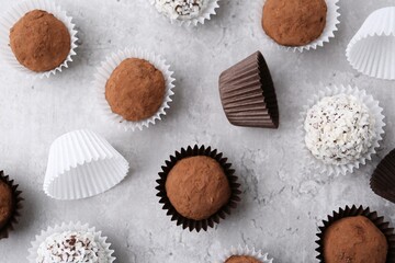 Delicious homemade candies with cocoa powder and coconut flakes on light grey table, flat lay