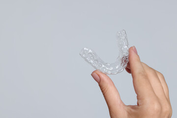 Woman with dental aligner on grey background, closeup. Space for text