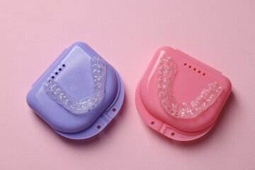 Clear aligners and colorful retainer cases on pink background, flat lay