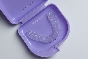 One clear aligner in retainer case on light grey background, top view