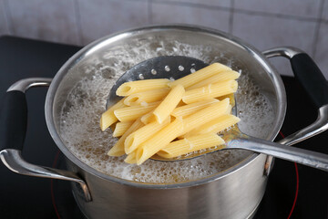 Taking cooked penne pasta from pot with boiling water on electric stove, closeup