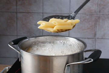 Taking cooked penne pasta from pot with boiling water on electric stove, closeup