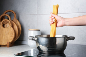 Woman putting tagliatelle pasta into pot on electric stove in kitchen, closeup