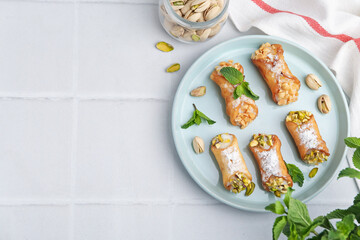Delicious cannoli with cheese, nuts and mint on white tiled table, flat lay. Space for text