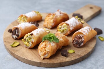 Delicious cannoli with cheese, nuts, powdered sugar, chocolate and mint on grey table, closeup