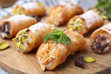 Delicious cannoli with cheese, nuts, powdered sugar, chocolate and mint on table, closeup