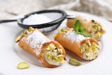 Delicious cannoli with cheese, pistachios, powdered sugar and mint on plate, closeup