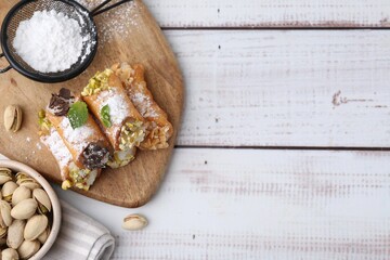 Delicious cannoli with cheese, nuts, powdered sugar, chocolate and mint on white wooden table, flat...