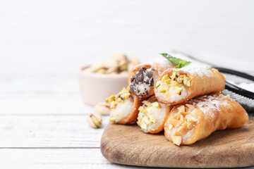 Delicious cannoli with cheese, nuts, powdered sugar, chocolate and mint on white wooden table, closeup. Space for text