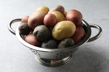 Different types of potatoes in colander on grey table, closeup