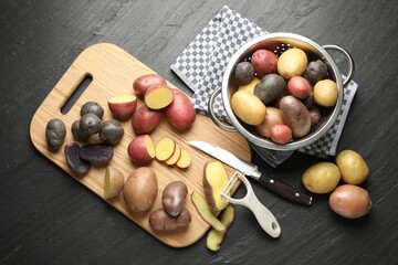 Different types of potatoes, peeler and knife on black table, flat lay