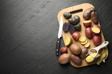 Different types of potatoes, peeler and knife on black table, flat lay. Space for text