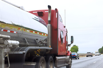 Large red truck with shiny fuel tank driving on highway during overcast weather