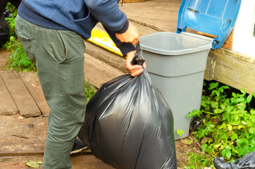 Man janitor puts garbage bag into plastic container.
