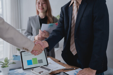 Two business people shaking hands after closing a deal in an office, a smiling businesswoman...