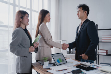 Business partners shaking hands in a bright, modern office after successfully negotiating a deal, surrounded by documents and a digital tablet on the table, exemplifying teamwork and collaboration