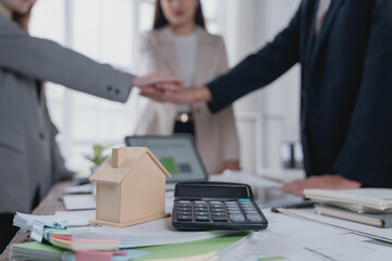 Real estate agents joining hands after closing a deal, with a miniature house and a calculator on...