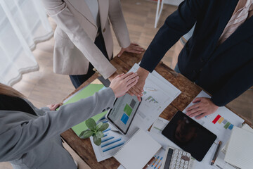 Business team joining hands over table with financial reports, celebrating successful teamwork and...