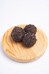 Three chocolate truffles covered with chocolate sprinkles served on a round wooden plate isolated...