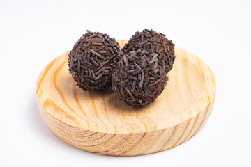 Three chocolate truffles covered with chocolate sprinkles served on a round wooden plate isolated on white background.