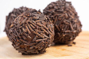 Three chocolate truffles covered with chocolate sprinkles served on a round wooden plate isolated on white background, close-up