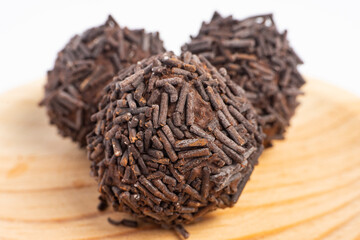 Three chocolate truffles covered with chocolate sprinkles served on a round wooden plate isolated...