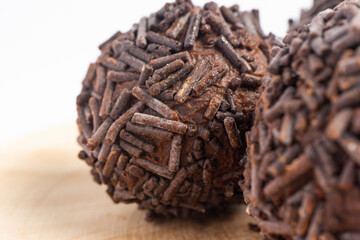 Three chocolate truffles covered with chocolate sprinkles served on a round wooden plate isolated on white background, close-up
