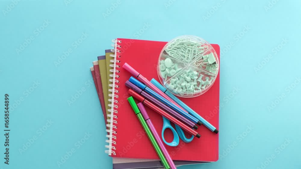 Poster a blue background with a red notebook and a green object on top of it. the notebook is open and has 