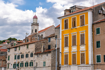 Fototapeta premium Cityscape of Sibenik, Croatia, featuring traditional terracotta roofs, wooden shutters, and a bell tower. Facade of a vibrant yellow building and the Church of St. Francis in the historic center