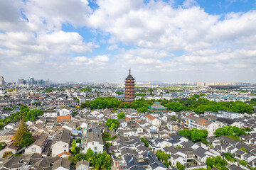 A cityscape with a tall pagoda tower stands amidst traditional houses and green trees under a...