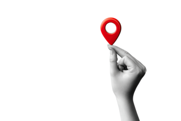 A grayscale hand holds a small, red location pin against a black background.  The pin is centered in the hand, with focus on the pin and hand