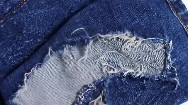 Close-up video showcasing the evolution of a ripped and frayed blue denim jeans texture