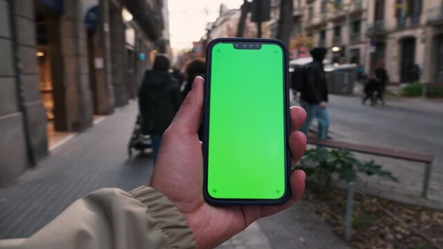 Man holds in hand smartphone with green screen mock up, using app. Urban life and leisure concept. 