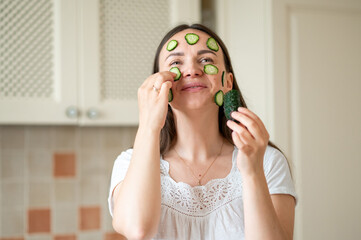 Woman with cucumber slices on her face enjoying a healthy skincare routine in a bright kitchen