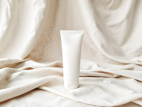 Minimal cosmetic tube mockup on soft fabric background, white lotion skincare packaging for branding, beauty product presentation and advertising.