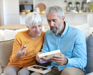 Portrait of a happy senior couple embracing eating chocolate praline from a gift box and having fun...