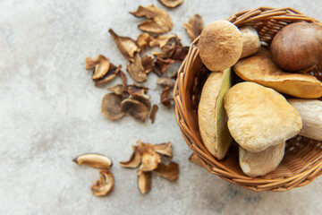 Fresh mushrooms overflowing from wicker basket onto table with dried mushrooms