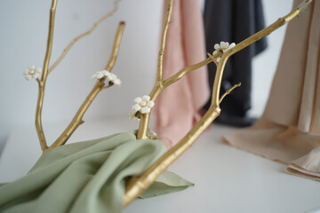 Close up of golden painted branches with small white flowers and green fabric on a white surface