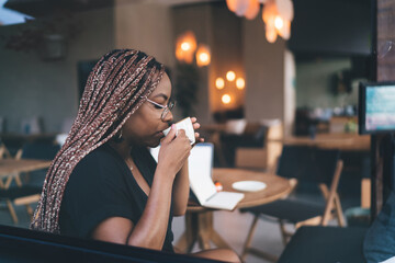 Serene African American woman sipping coffee mid-task, embodying peaceful balance between digital work and self-care in tech-enhanced freelance environment.