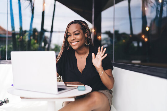 Black freelancer smiles and waves during video call, expressing professionalism, digital connectivity, and personal touch in remote business communication.