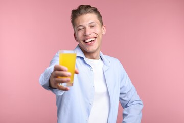 Happy man with glass of orange juice on pink background. Refreshing drink