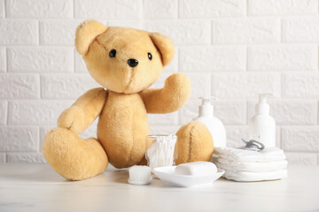 Many different baby accessories and toy bear on table near brick wall