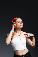 Beautiful woman in stylish bijouterie, headphones and top posing on dark grey background