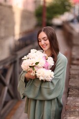 Charming woman with bouquet of beautiful peonies on city street