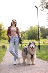 Happy woman walking with her cute Alaskan malamute dog in park