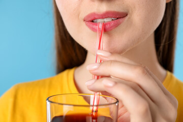 Woman drinking juice through straw on light blue background, closeup